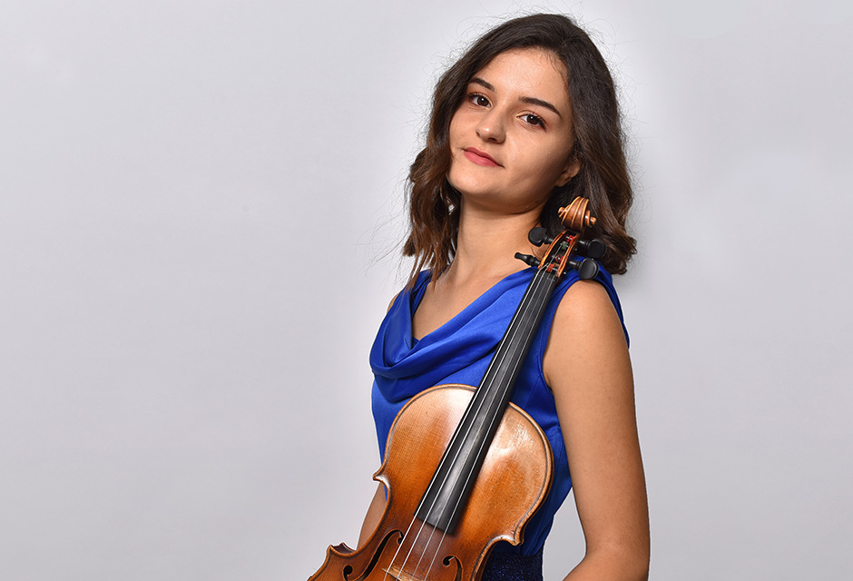 RCM violinist Jelena Horvat is pictured against a plain grey background, wearing dark blue, and holding her instrument.